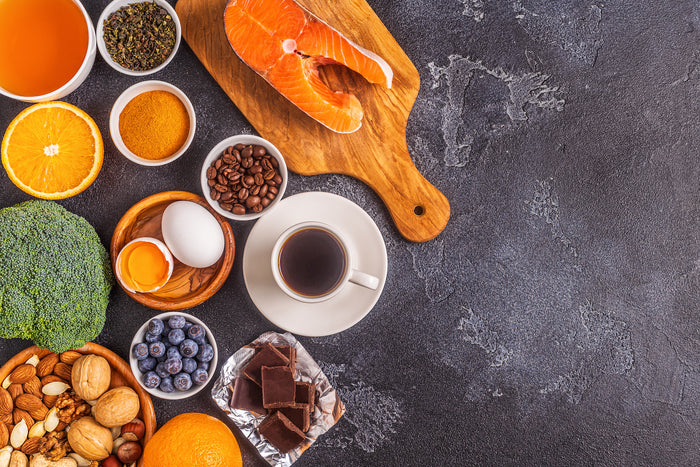 Top-view-of-brain-boosting-foods-on-a-dark-background-coffee-salmon-coffee-beans-egg-orange-turmeric-green-tea-broccoli-nuts-blueberries-and-dark-chocolate.
