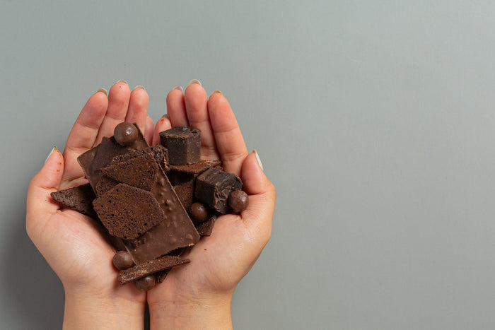 Hands-holding-assorted-dark-chocolate-pieces-on-a-neutral-background.