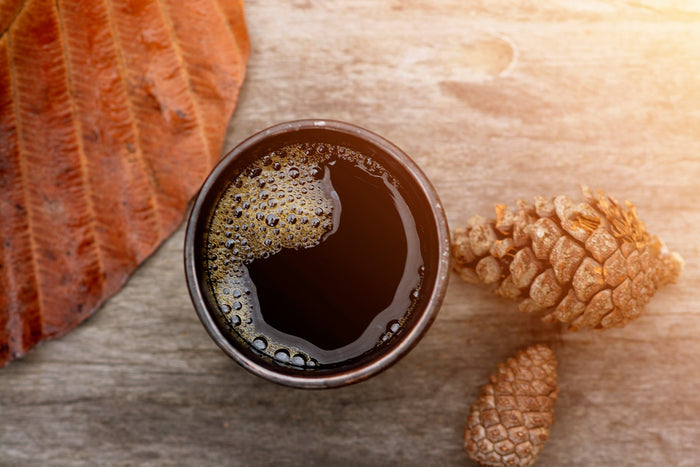 Steaming a cup of black coffee with pinecone and dried leaves on a wooden surface