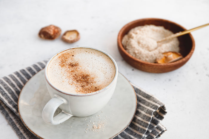 Maca-coffee-with-cinnamon-served-on-a-ceramic-saucer-with-maca-powder-in-a-wooden-bowl-nearby.