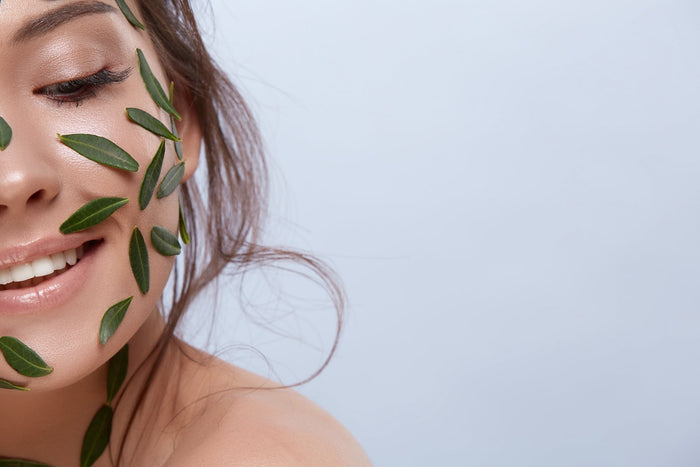 :A woman smiling, with some leaves on her smooth skin, symbolizing natural skincare