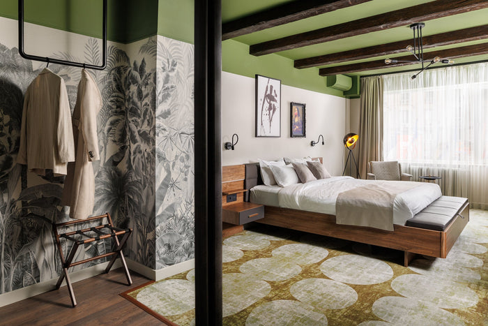 Stylish hotel room with wooden bed, patterned carpet, wall art, and natural light from a large window.
