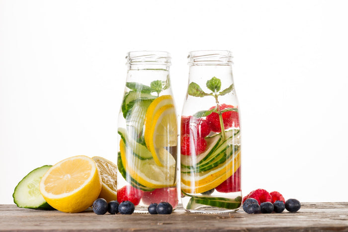 Bottles of detox water with lemon, cucumber, berries, and mint.
