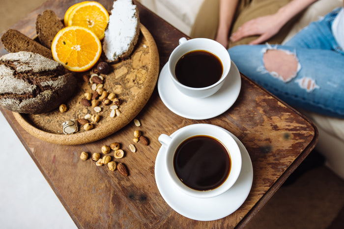 two-cups-of-black-coffee-and-a-plate-featuring-slices-of-bread-oranges-nuts-and-seeds-natural-sources-of-B-vitamins.