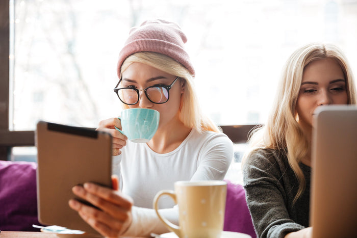 Two young women drinking coffee and using tablet in a café