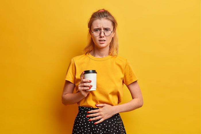 unhappy female frowns face feels unwell keeps hand on belly drinks takeaway coffee